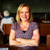 grok-image-remove the ......, she is sitting smiling at the table, arms folded, do not alter he...jpg